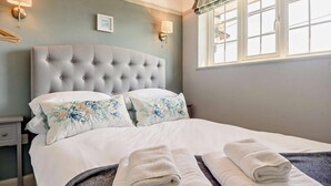 A neatly made bed with floral pillows, a tufted headboard, and two bedside lamps. - 3 Bed in Southwold (oc-s27351) (Southwold)