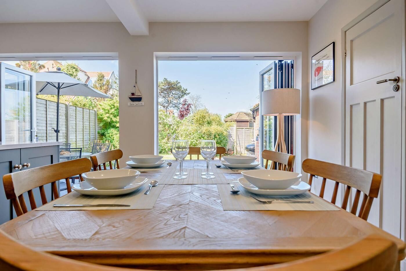 Uma sala de jantar com uma mesa posta para quatro pessoas, cadeiras e vista para o jardim através de grandes janelas.