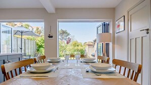A dining area with a table set for four, chairs, and a view of the garden through large windows. - 3 Bed in Southwold (oc-s27351) (Southwold)