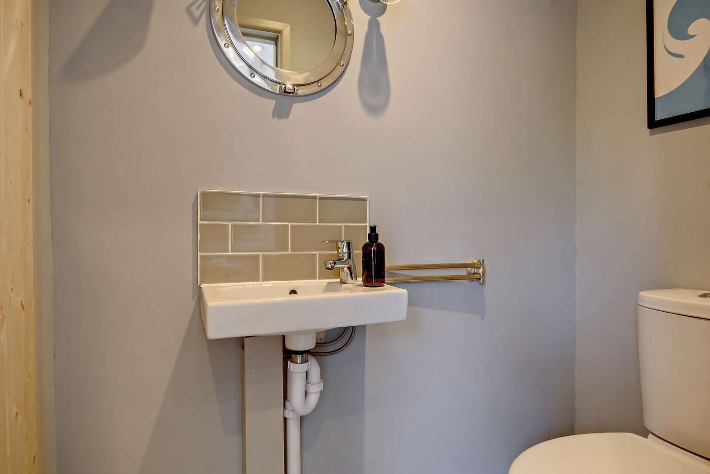 Une salle de bain avec un lavabo blanc, un miroir rond et des toilettes.