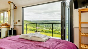 Een slaapkamer met een groot bed, een houten stoel, een televisie en uitzicht op het landschap.