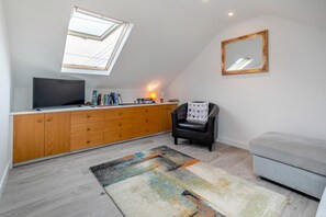 A modern living room with a TV, wooden cabinet, black leather chair, grey sofa, and a colorful rug. - 1 Bed in Helston (oc-a27352) (Helston)
