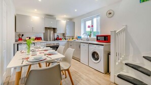 A modern kitchen with white cabinets, a dining area with a table set for two, and a washing machine. - 1 Bed in Helston (oc-a27352) (Helston)