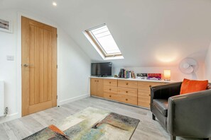 A compact living space with a loft bedroom, a television, a sofa, and a small table with books and a lamp. - 1 Bed in Helston (oc-a27352) (Helston)