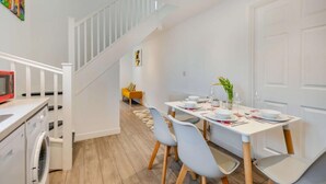 A modern kitchen with a washing machine, a dining area with a table set for four, and a staircase leading to another room. - 1 Bed in Helston (oc-a27352) (Helston)