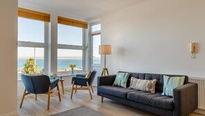 Ett vardagsrum med ett stort fönster, en golvlampa och en soffa med många kuddar.