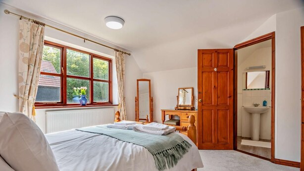 Une chambre à coucher comprenant un lit, une commode, un miroir, une fenêtre avec des rideaux et une porte donnant sur une salle de bain.