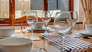 Une table à manger dressée avec de l’assiette blanche, des bols et des verres à vin, avec une chaise en bois et une fenêtre en arrière-plan.