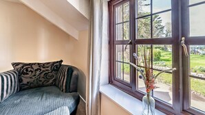 Una habitación con ventana, sofá y un florero con flores.