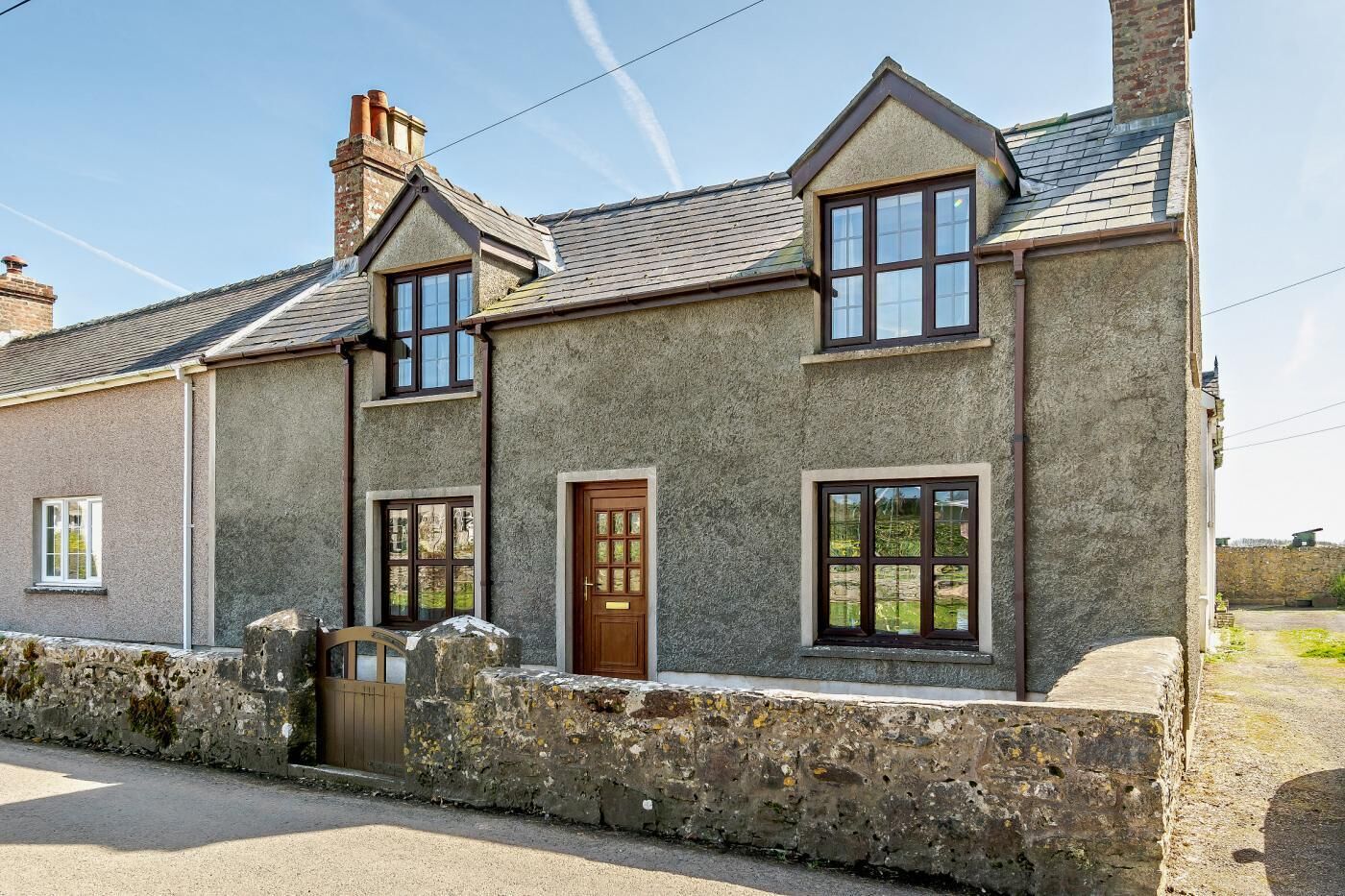 A two-story stone house with a traditional design, featuring a stone wall foundation, a wooden door, and multiple windows.