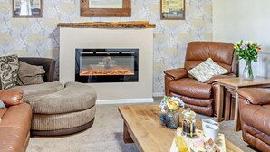 Una sala de estar con chimenea, sofás de cuero, una mesa de centro con alimentos para el desayuno y decoración en la pared.