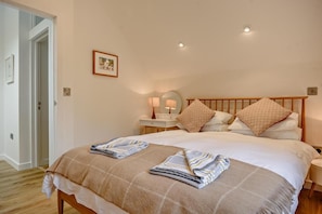 A bedroom with a large bed, two bedside tables, a nightstand, a mirror, and a framed picture on the wall.