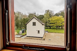 A view through a window of a small white building with a gabled roof, surrounded by trees and a gravel area.