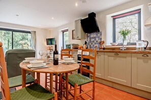 A dining area with a round table, chairs, and a wine bottle. There is a kitchen with a stove, sink, and cabinets.