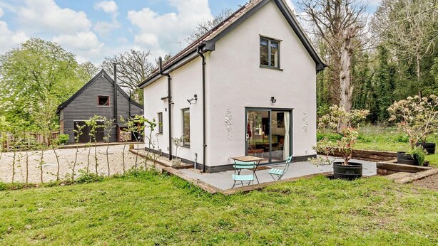 Een tweelaags huis met een terras, een kleine tuin en een aangrenzend gebouw.