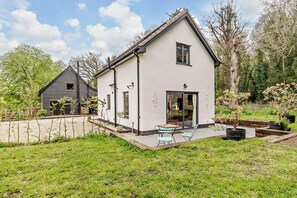 Une maison à deux étages avec un patio, un petit jardin et un bâtiment voisin.