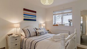 A bedroom with a bed, bedside tables, a lamp, a window with a view, and a decorative wall piece. - 2 Bed in Southwold (oc-p27380) (Southwold)