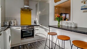 A modern kitchen with a built-in oven, a coffee maker, and a toaster. There are three stools at the counter. - 2 Bed in Southwold (oc-p27380) (Southwold)