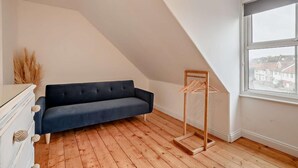 Una habitación con un sofá azul oscuro, un perchero de madera y una ventana con vistas a edificios.