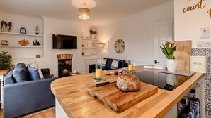 Una sala de estar moderna con una mesa de centro de madera, chimenea, televisor y comedor con mostrador de cocina.