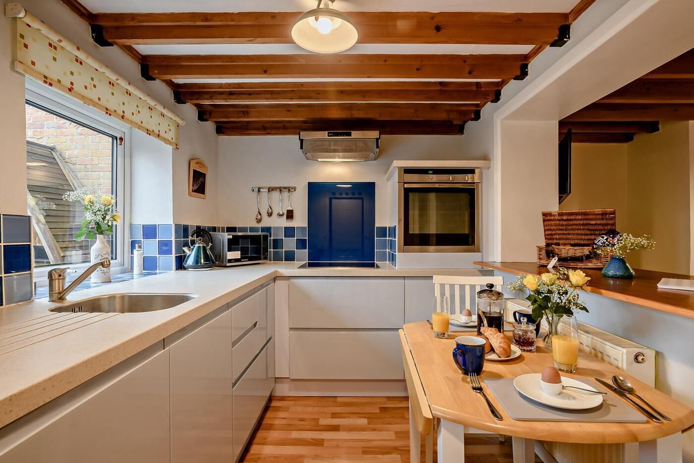 A modern kitchen with a wooden ceiling, a blue door, and a dining area with a table set for two.