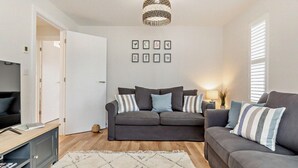 Ein modernes Wohnzimmer mit einem grauen Sofa, einem Fernseher und einer dekorativen Lampe.