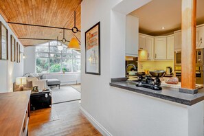Une cuisine moderne avec un plafond en bois, un coin repas comprenant une table et des chaises, et une vue sur l’extérieur grâce à de grandes fenêtres.