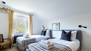 Ein Schlafzimmer mit zwei Betten, einem Fenster mit Vorhängen, einem Heizkörper, einem Stuhl und einem gerahmten Bild an der Wand.