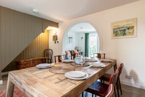 Un coin repas avec une longue table en bois dressée pour quatre personnes, un escalier et un tableau accroché au mur.