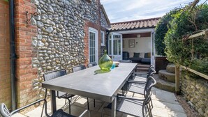 Eine Terrasse im Freien mit einer Steinmauer, einem Tisch mit Stühlen und Blick auf ein Haus mit Ziegeldach.