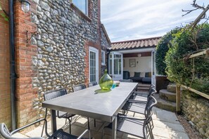 Une terrasse extérieure avec un mur en pierre, une table avec des chaises et une vue sur une maison avec un toit en tuiles.