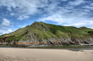 A beach with a grassy hill and rocky cliffs. - 2 Bed in Mumbles (oc-t27408) (The Mumbles)
