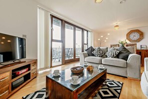 Ein Wohnzimmer mit Fernseher, Sofa, Couchtisch und Blick durch große Schiebetüren.