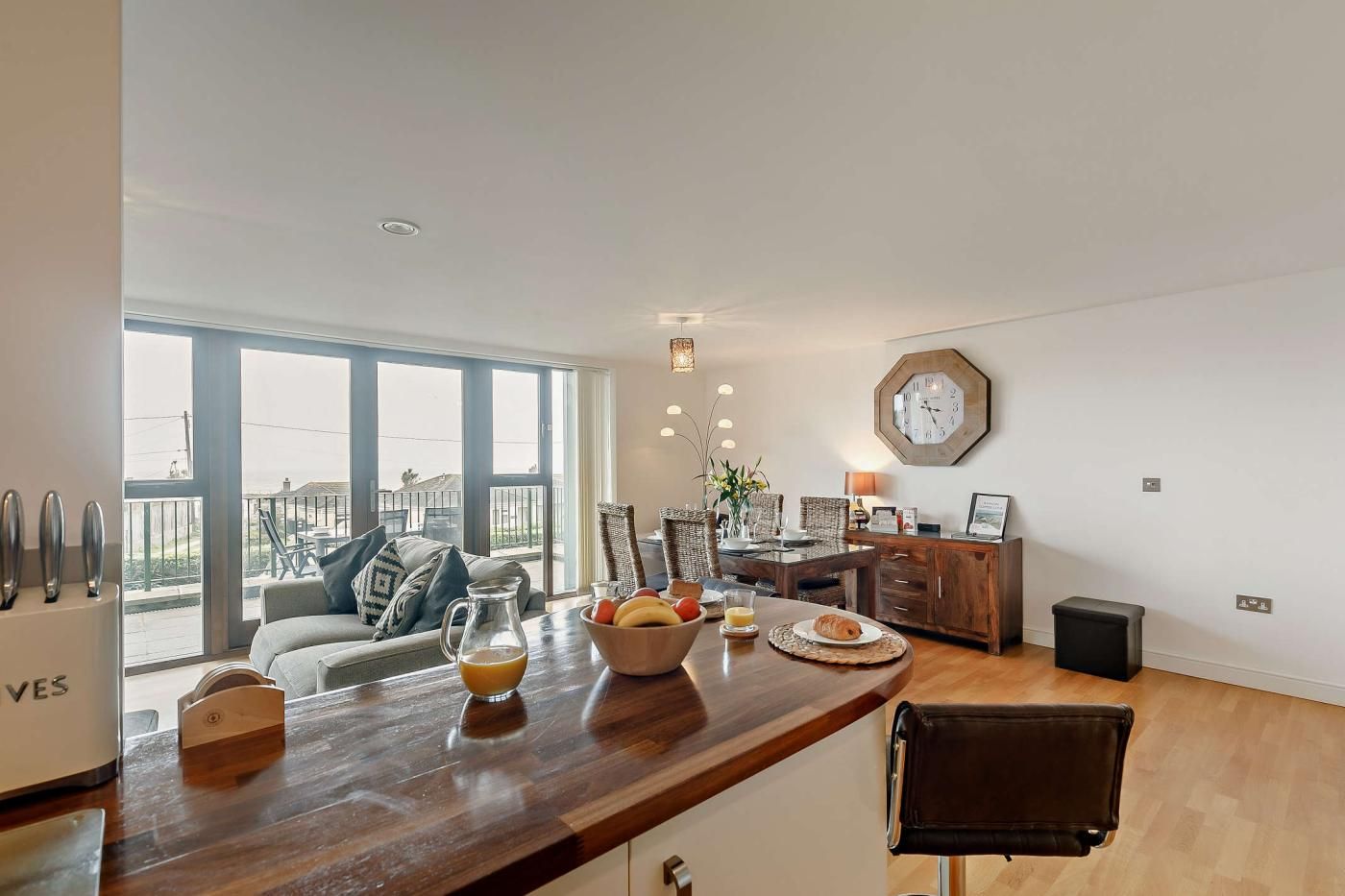 A modern kitchen with a wooden countertop, a dining area with wicker chairs, and a large window offering a view of the outdoors.