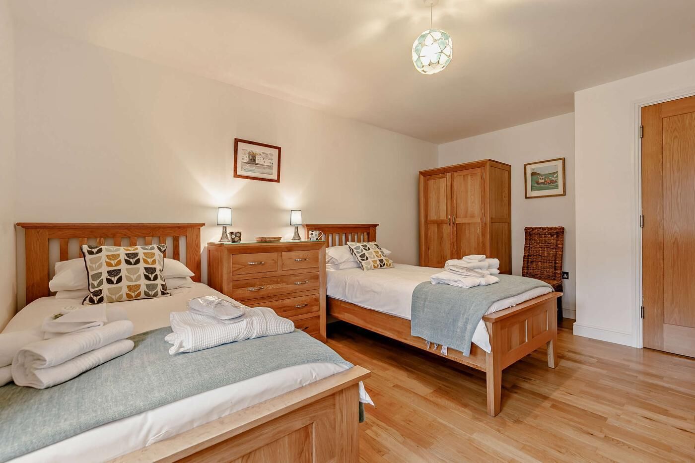 Habitación de hotel con dos camas de madera, un armario de madera, una cómoda de madera y una única lámpara.