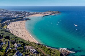 An aerial view of a coastal town with a beach, clear blue waters, and a small island with a lighthouse. - 1 Bed in St. Erth (oc-c27438) (Saint Erth)