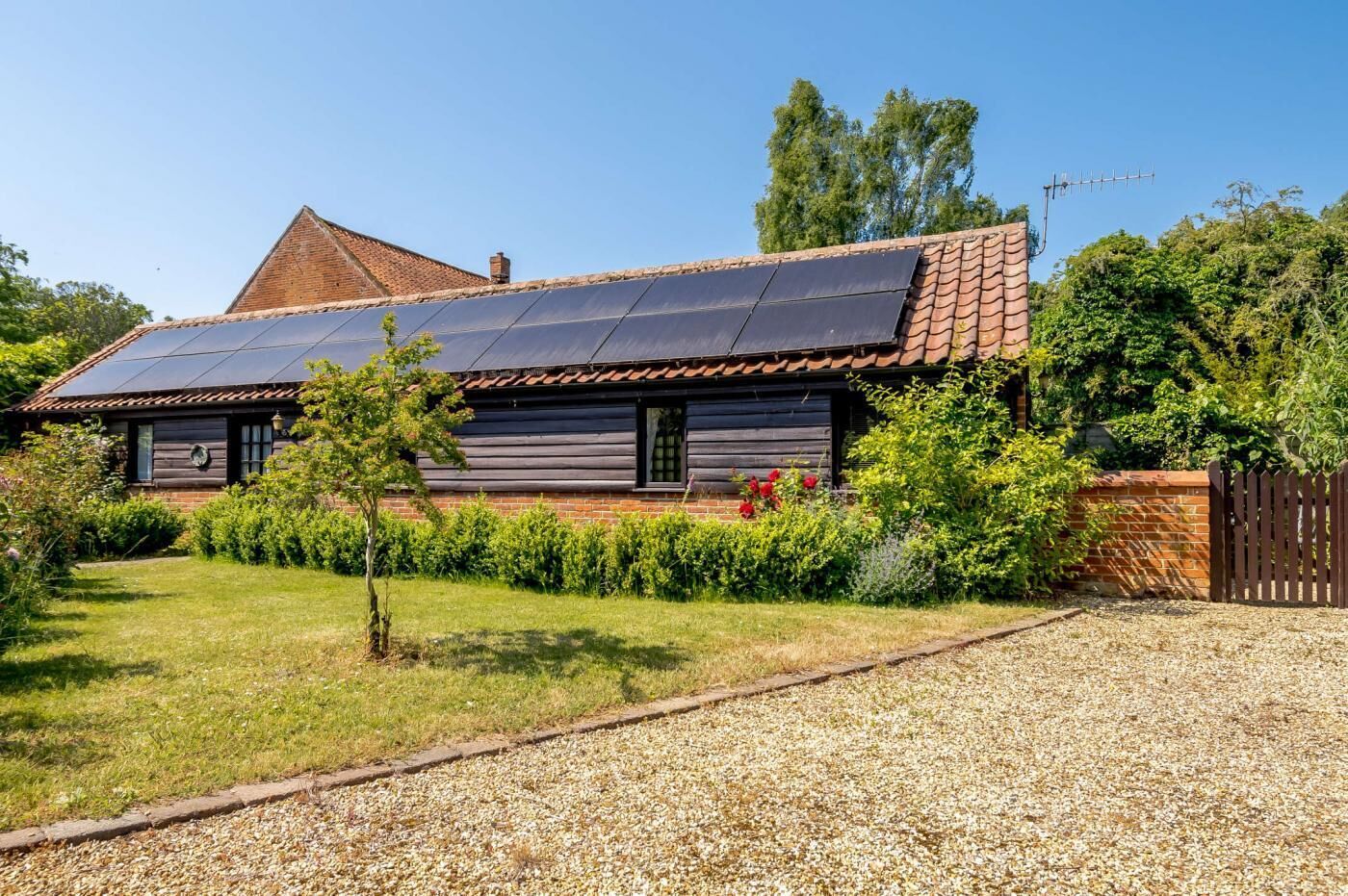 Een huis met schuin dak, zonnepanelen, een houten gevel en een grindpad.