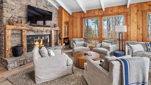 A cozy living room with a stone fireplace, comfortable seating, and large windows offering a view of the outdoors. - Ski-In/Out Lodge | Stratton Mountain (Stratton)
