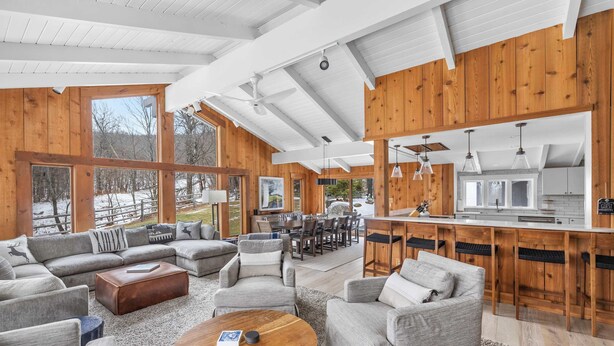 A spacious living area with a large sofa set, a coffee table, and a kitchen area with bar stools. - Ski-In/Out Lodge | Stratton Mountain (Stratton)