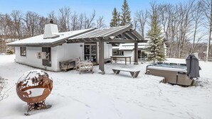 A snow-covered outdoor area with a hot tub, a wooden bench, and a metal sculpture. - Ski-In/Out Lodge | Stratton Mountain (Stratton)