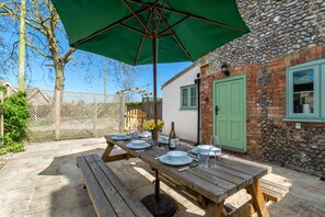 An outdoor wooden table set with plates, glasses, and a bottle, under a green umbrella, with a stone wall and a green door in the background. - 3 Bed in Kelling (oc-w27424) (Kelling)