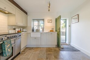 A compact kitchen with a built-in oven, a sink, and a window with a floral curtain. - 3 Bed in Kelling (oc-w27424) (Kelling)