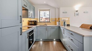 A modern kitchen with grey cabinets, a stainless steel range hood, a built-in oven, and a window with a view of the street. - 2 Bed in Sheringham (oc-b27372) (Sheringham)