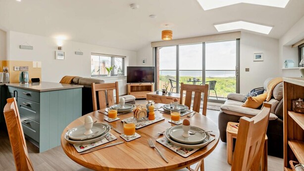 A modern kitchen with a dining area, a TV, and a large window overlooking a scenic view. - 2 Bed in Sheringham (oc-b27372) (Sheringham)