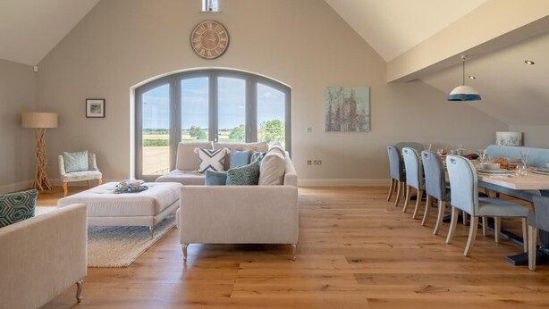 Un ampio loft con soffitto alto, zona pranzo con tavolo e sedie, angolo salotto accogliente con divano e poltrone, e un'ampia finestra ad arco che offre vista sulla campagna.