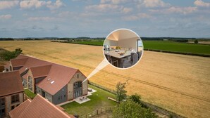 Una proprietà rurale con un ampio campo aperto, una casa con tetto in tegole rosse e una rientranza circolare che mostra una cucina moderna con zona pranzo.