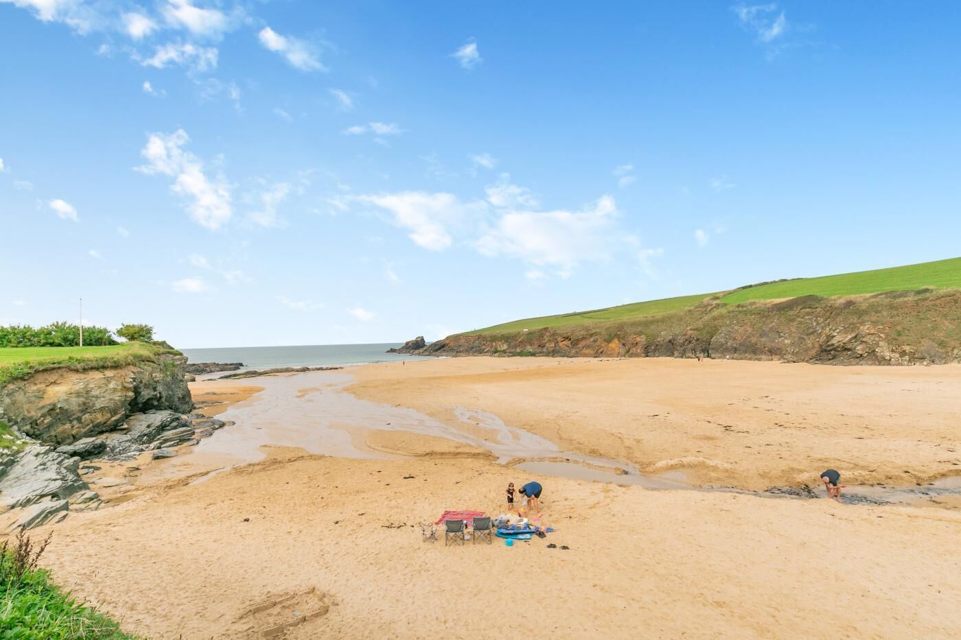 Une plage avec un ciel dégagé, des falaises rocheuses et une colline verdoyante en arrière-plan.