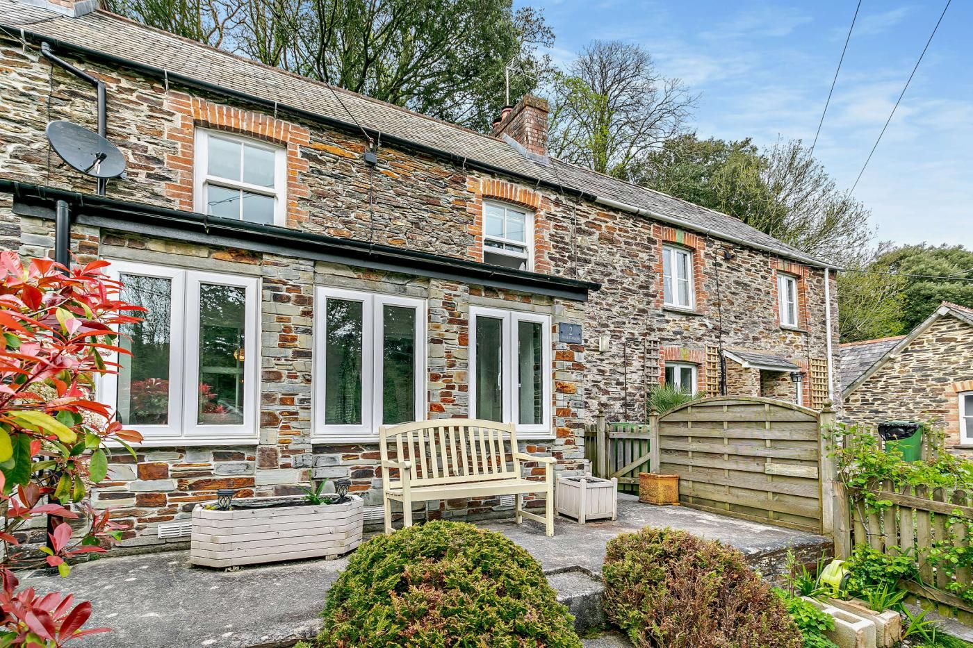 A stone house with multiple windows, a wooden bench, and a garden area.