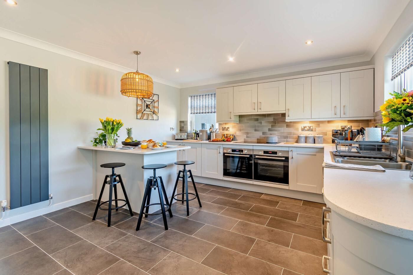 A modern kitchen with white cabinets, a central island with stools, a hanging light fixture, and a built-in oven.