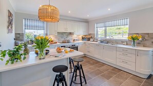 Een moderne keuken met witte kastjes, een centraal eiland, barstoelen en een hanglamp.